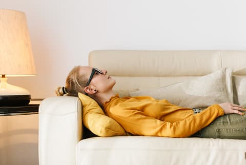 Side view of young woman lying dreamily on cozy couch keeping eyes closed and thinking