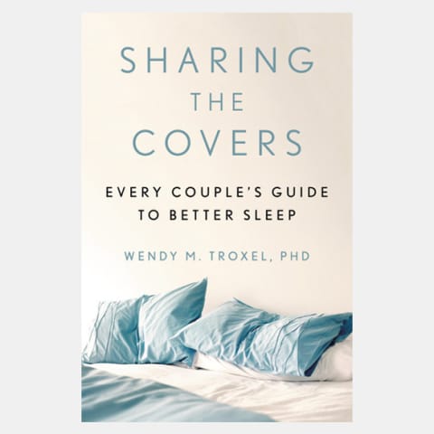 White book cover titled Sharing The Covers with a picture of a bed with blue pillows and blanket.
