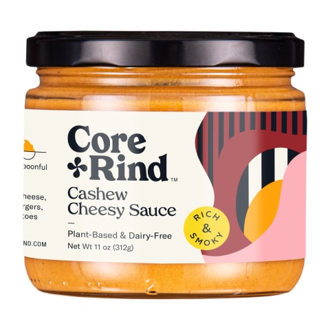 Core + Rind glass jar of cashew cheesy sauce with rich and savory flavored. Orange cheese dip inside with a black lid.