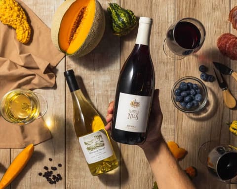 two bottles of wine held over table with grapes and fruit