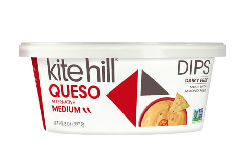 White queso tub from Kite Hill image of orange queso with a tortilla chip on top, vegan queso.