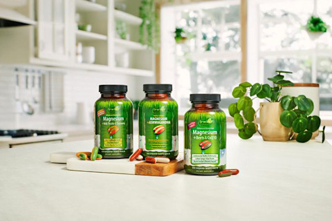 Three green bottles of Irwin Naturals supplements are displayed on a white kitchen counter against a brightly lit window background. The products shown are Magnesium + Ashwagandha, Magnesium + Zinc Oxide & Trace Elements, and Advanced Absorption Magnesium + Beets & CoQ10. A few liquid soft-gel capsules are scattered on a wooden cutting board next to the bottles, and a potted plant sits nearby. Three green bottles of Irwin Naturals supplements are displayed on a white kitchen counter against a brightly lit window background. The products shown are Magnesium + Ashwagandha, Magnesium + Zinc Oxide & Trace Elements, and Advanced Absorption Magnesium + Beets & CoQ10. A few liquid soft-gel capsules are scattered on a wooden cutting board next to the bottles, and a potted plant sits nearby.