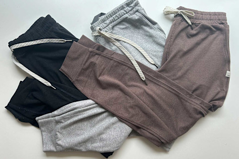 three pairs of vuori joggers folded on a blue background