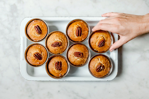 Hand reaching for homemade muffins in muffin tin on marble background Hand reaching for homemade muffins in muffin tin on marble background