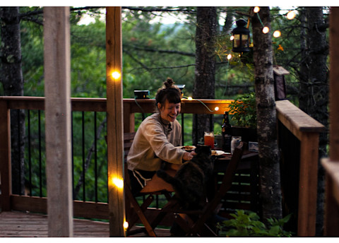 woman and cat eating dinner on porch of remote cabin woman and cat eating dinner on porch of remote cabin