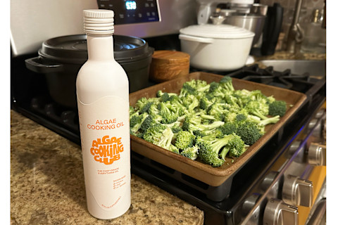 Algae Oil on countertop next to broccoli in tan plate on stove