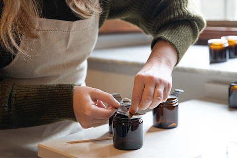 White woman wearing green sweater and tan apron adding the wick to homemade candle White woman wearing green sweater and tan apron adding the wick to homemade candle