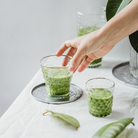Hand Reaching for a Glass of Green Juice Hand Reaching for a Glass of Green Juice