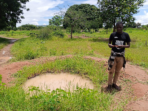 man standing next to a small, dirty pond in grassy field man standing next to a small, dirty pond in grassy field