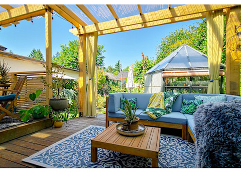 Backyard patio with blue rug, brown table, plants, and a blue couch
