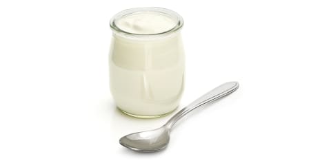 glass jar of plain greek yogurt with spoon over white background