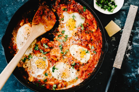 Shakshuka in an iron skillet with parmesan cheese and a cheese grater