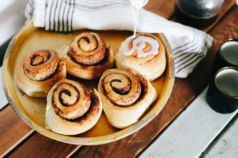 Pouring Icing On Cinnamon Buns On Wooden Table