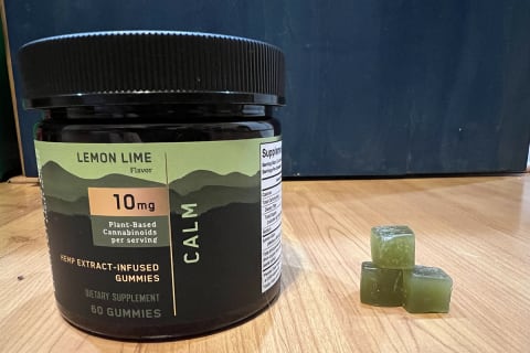 Charlottes Web Calm Gummy on wood floor next to stack of three green gummies
