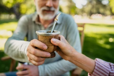 older couple passing a cup of yerba mate back and forth in a park