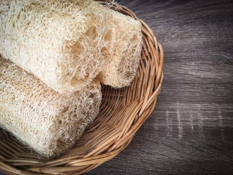 Dry loofah sponge in cane bowl on brown table