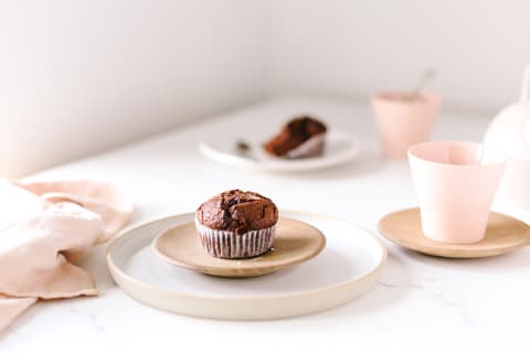 Chocolate muffin on wood plate and white ceramic plate with fork on a table sprinkled with sea salt and accompanied with tea