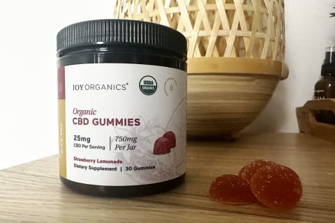 Joy organics broad-spectrum cbd gummies on desk next to stack of gummies