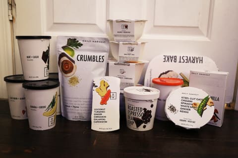 Items in a Daily Harvest box including 4 smoothies, 2 crumbles, 1 scoops dessert, 2 bowls, 2 meal bowls, a bake, latter, and almond milk