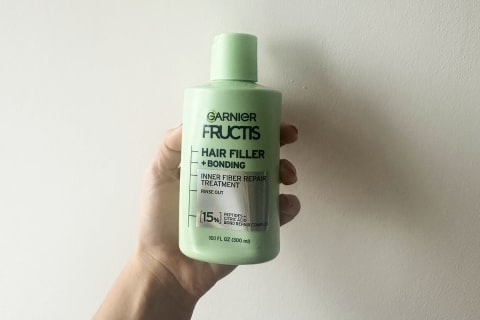 Garnier Fructir Hair Filler Bonding Fiber Repir Treatment Green Bottle in hand held against wall