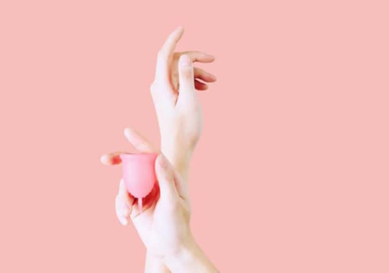 hands holding a pink menstrual cup in front of pink wall