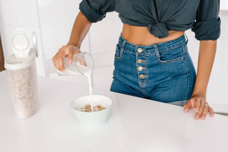 匿名女性休闲装倒鲜奶放入碗内谷物玉米片，同时准备在家里的健康早餐立即下载必威手机版APP