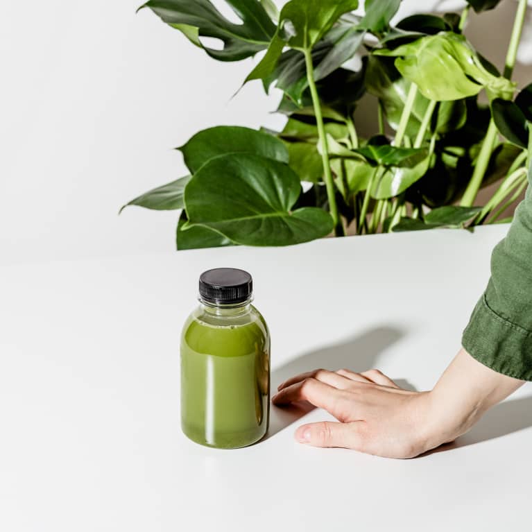 Hand Beside a Bottle of Green Juice on a White Table