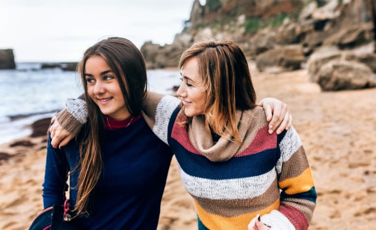 Woman / mom with her arm around her teenage daughter outside on the beach during fall / winter! Woman / mom with her arm around her teenage daughter outside on the beach during fall / winter!