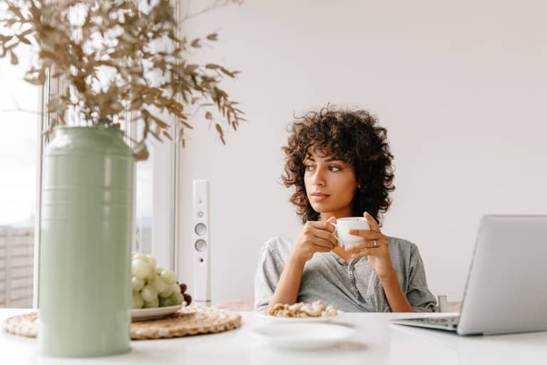 ady with cup of hot drink sitting at table and looking away in morning at home