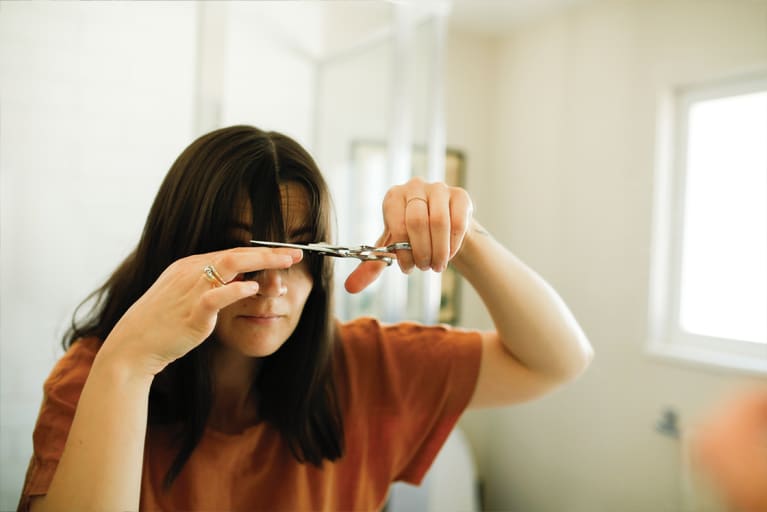 woman cutting her bangs in the mirror