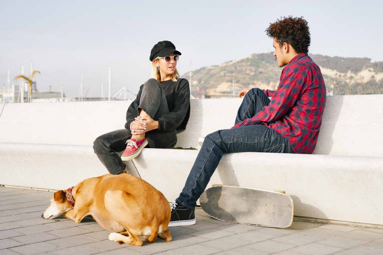 两个朋友和一条狗坐在户外的长凳上