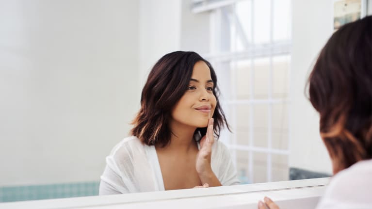 woman looking in mirror applying skincare