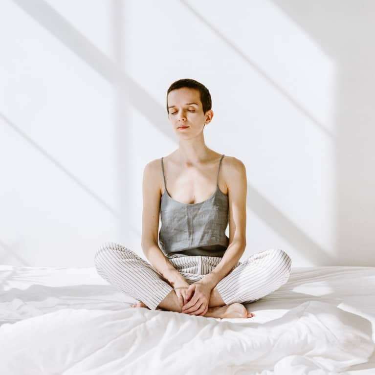 Young woman sitting on a bed with her eyes closed meditating