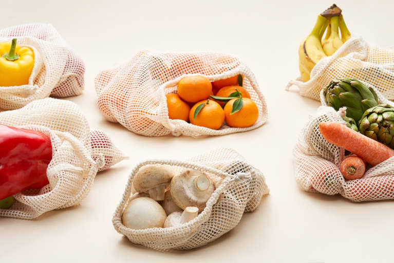 各种新鲜水果和蔬菜中的可重复使用的棉布袋放在奶油背景