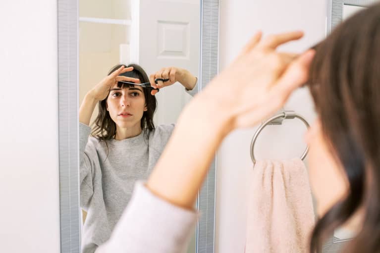 Young Woman Cutting Bangs In Mirror At Home