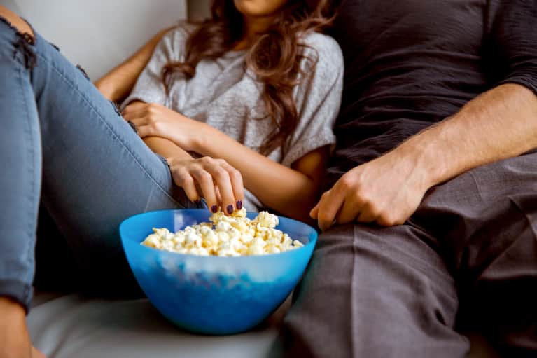 Couple sitting on couch and snacking on popcorn together