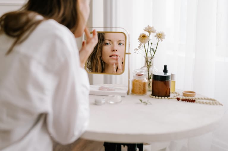 woman sitting at a vanity applying lip balm in mirror