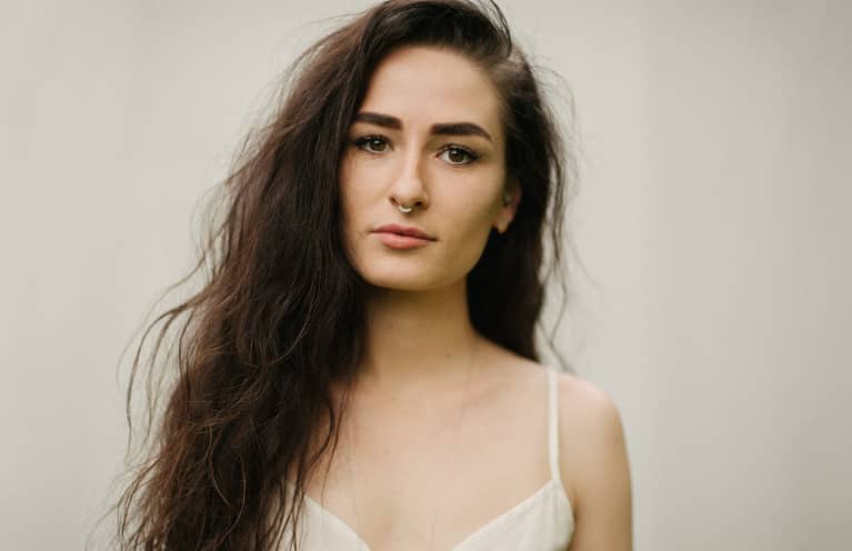 Female With Long Curly Dark Hair And Septum Nose Piercing With Cream Background And Cream Romper