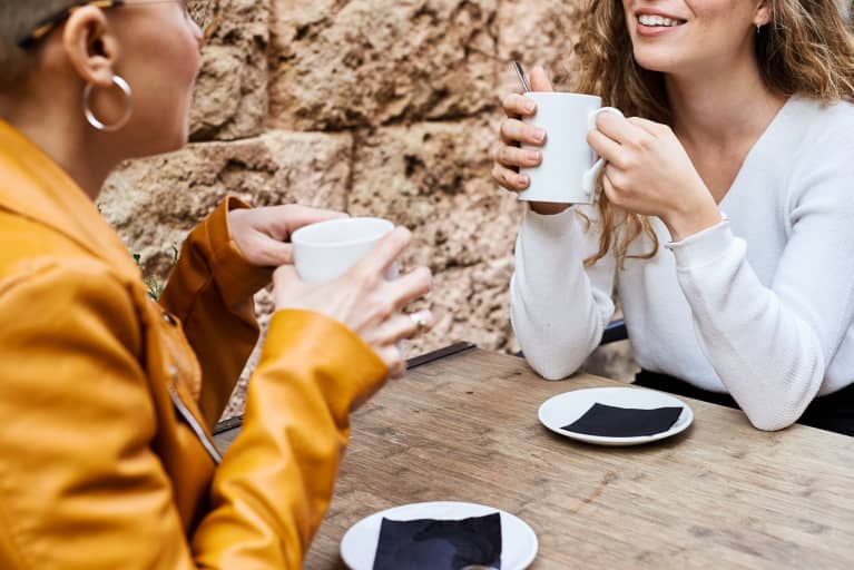Unrecognizable female friends having cup of tea in bar terrace while having conversation