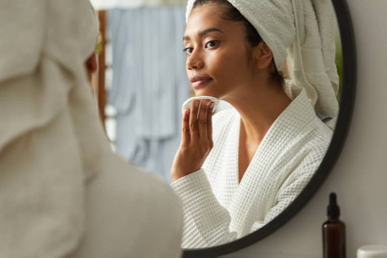 Woman in bathroom removing her make up while looking at the mirror in skincare morning routine at home