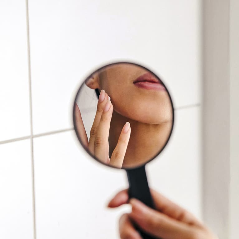Woman Applying Skin Cream in a Handheld Mirror