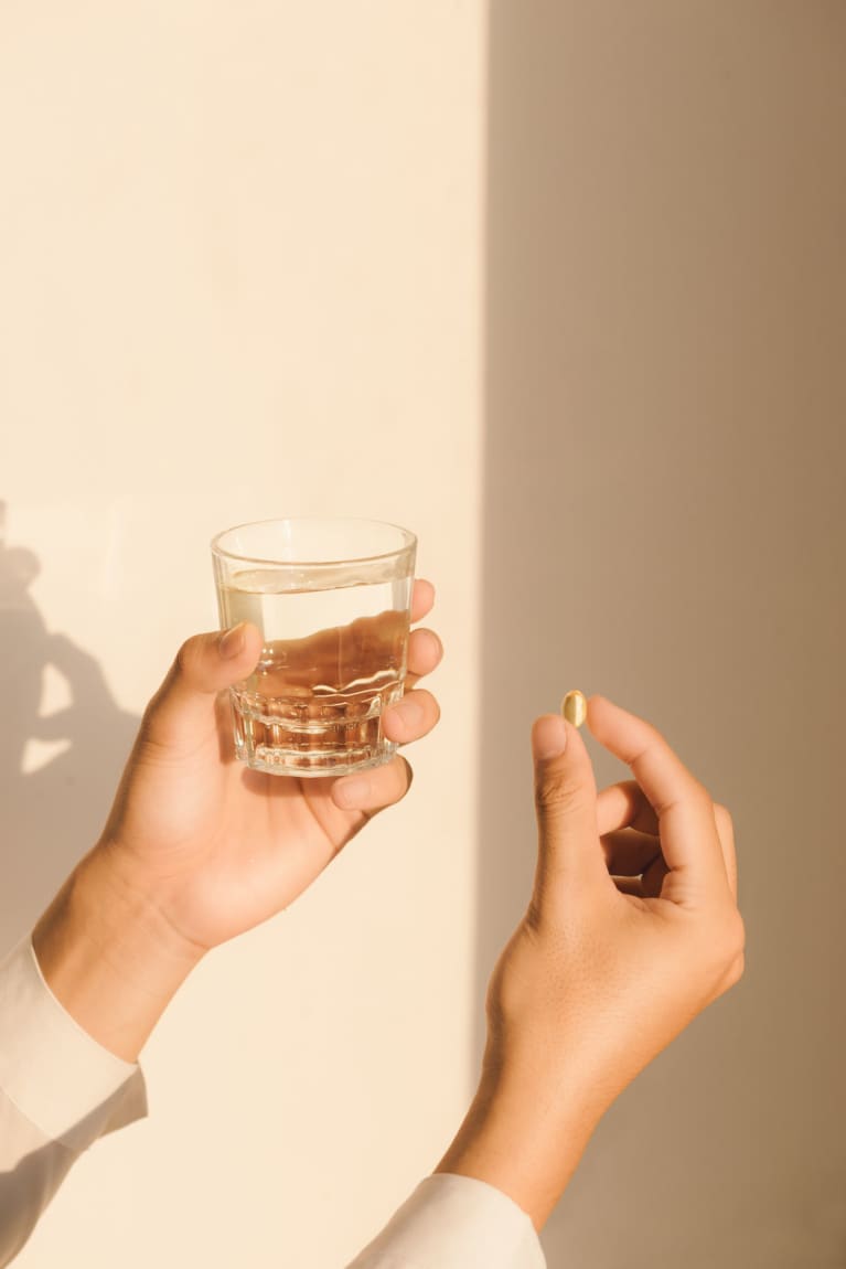 Someone Holding a Glass of Water and a Supplement