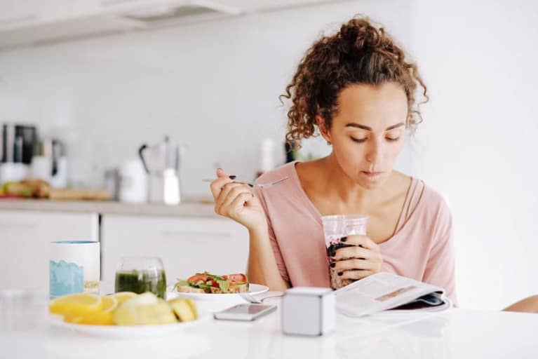 woman eating breakfast and reading in kitchen