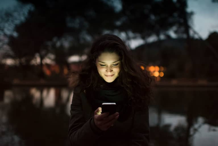 Portrait of a smiling woman using smartphone with happy face expression illuminated by the light of the device