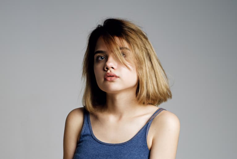 Portrait of beautiful teen girl in blue crop top and grey skirt embracing herself with hand and looking at camera