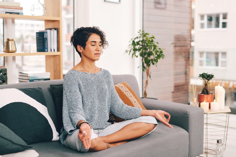 young woman sitting and meditating on her sofa in the living room