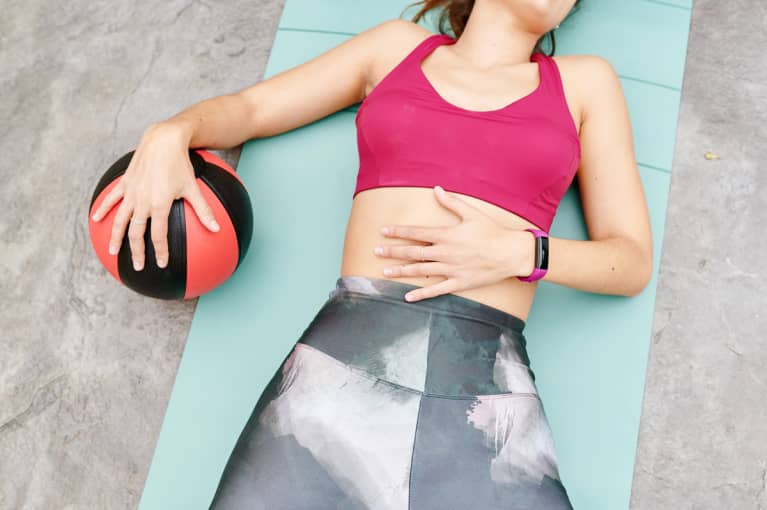 Unrecognizable woman in sportswear lying on an exercise mat with a ball after an outdoor workout