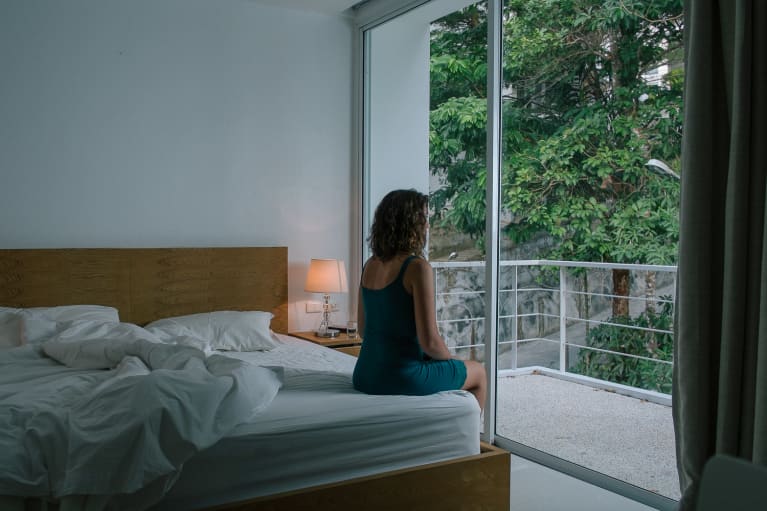 Woman in a nightgown sitting on bed facing window on a dark early morning Woman in a nightgown sitting on bed facing window on a dark early morning