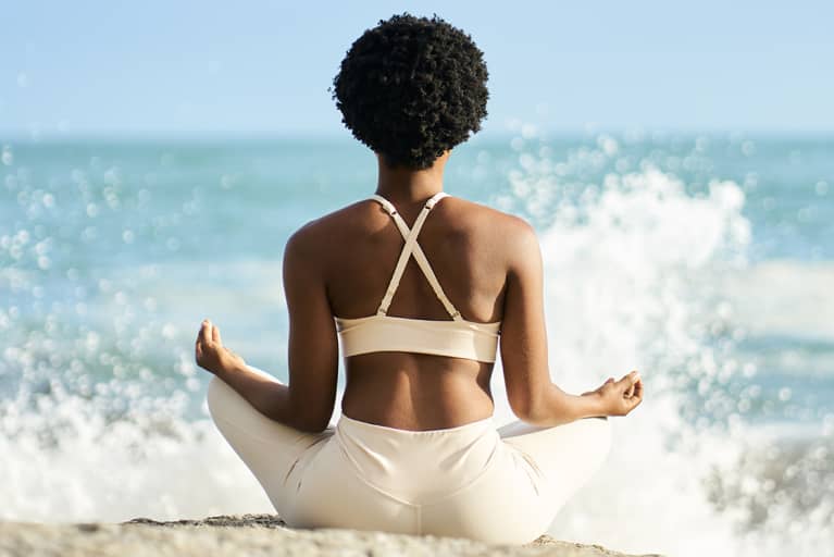 woman meditating outdoors on some oceanside rocks