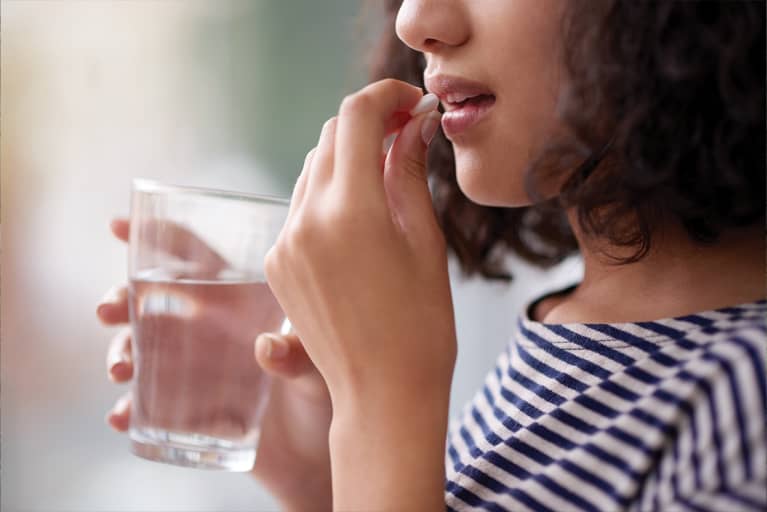 woman holding glass of water taking pill